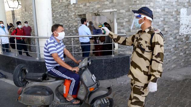 A paramilitary officer checks the temperature of worker at the entry gate of the airport in Jammu.(Nitin Kanotra / Hindustan Times) A paramilitary officer checks the temperature of worker at the entry gate of the airport in Jammu.(Nitin Kanotra / Hindustan Times)