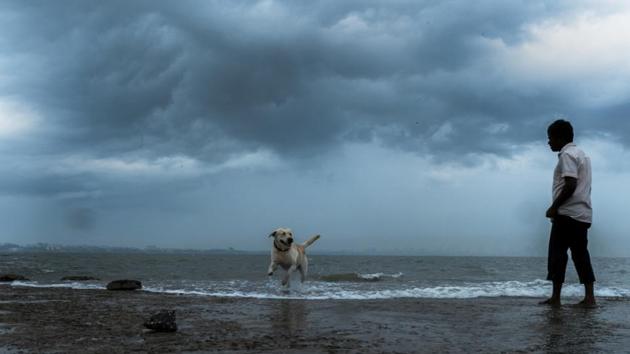 A man plays with his pet dog as black cloud hovers over Mumbai skyline at Madh Island, Malad. (Photo by Samson Tupdal/HT PHOTO)