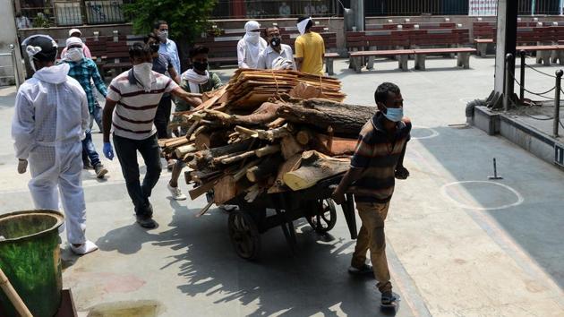 Workers pull a cart loaded with wood that is fed into traditional cremation pyres. Funerals these days begin at 8.00am and go on late into the night at the cremation ground. (Sajjad Hussain / AFP)