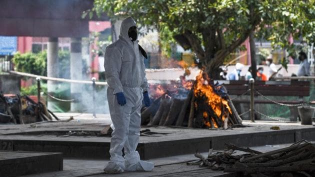 A relative wearing PPE coveralls stands in front of a burning pyre. Only three of the six furnaces at Nigambodh Ghat are currently working, so for the past week wood pyres, the traditional structures used in Hindu funeral rituals for thousands of years have been allowed to help clear the backlog. (Sajjad Hussain / AFP)