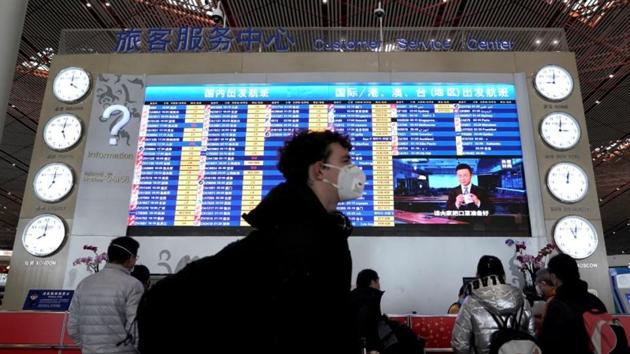 FILE PHOTO: A foreign traveller wearing a mask walks past a departures information board at Beijing Capital International Airport in Beijing