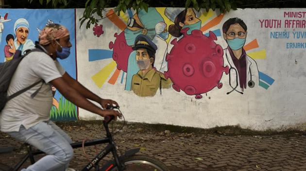 A man wearing a mask pedals his bicycle past a graffiti on a wall made to create awareness about the coronavirus in Kochi, Kerala.(AP) A man wearing a mask pedals his bicycle past a graffiti on a wall made to create awareness about the coronavirus in Kochi, Kerala.(AP)