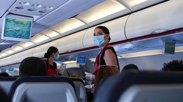 A cabin crew member wearing a protective facemask serves passengers aboard a flight to the island of Santorini in Greece on June 13. A ban on flights from Italy, Spain and the Netherlands has been lifted, although one on flights from Britain remains in place. (Aris Messinis / AFP)