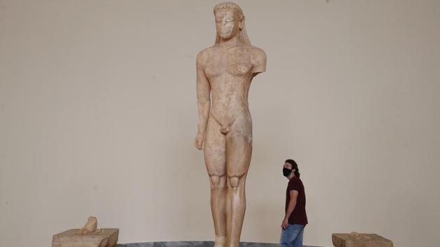 A visitor seen wearing a face mask to prevent the spread of the new coronavirus, looks at the 600 B.C. Naxian marble statue of a Kouros during the reopening of the Archaeological Museum in Athens. (Thanassis Stavrakis / AP)