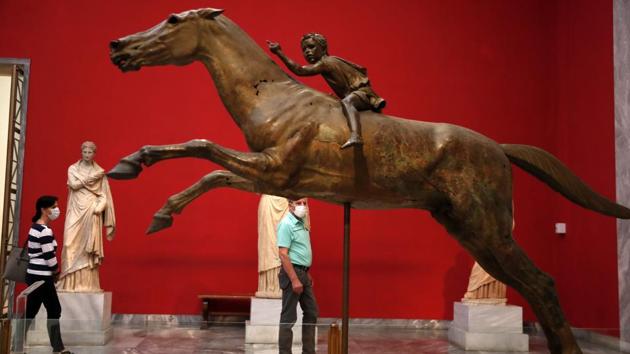 A couple wearing face masks look at the 140 B.C. bronze statue of a young jockey riding a horse during the reopening of the Archaeological Museum in Athens on June 15. The easing of restrictions also unlocks access to the troves of priceless historical treasures in the country’s museums and galleries. (Thanassis Stavrakis / AP)