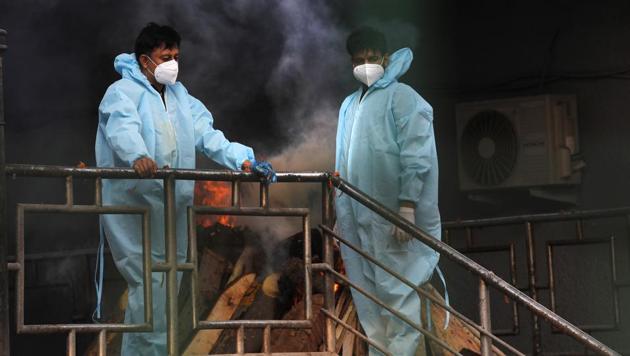 People wait by the burning pyre of a relative who died of Covid-19, at a crematorium in New Delhi, India.(AP)