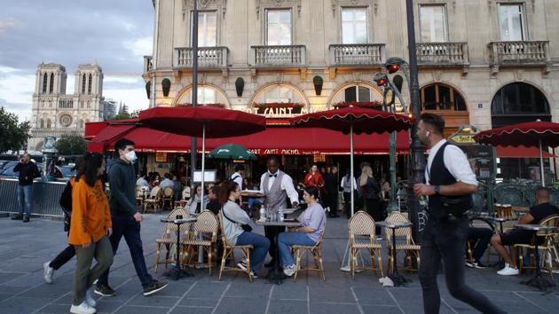 A waiter, center, clears a table in a restaurant with Notre Dame Cathedral in the background, Monday, June 15, 2020 in Paris. Paris is rediscovering itself, as its cafes and restaurants reopen for the first time since the fast-spreading virus forced them to close their doors March 14. Restaurants outside the Paris region opened earlier this month, and Paris cafes were allowed to serve people outside but not open their doors. After three months of losses, some restaurateurs fear it will take a long time for business to come back. (AP Photo/Thibault Camus) (AP)