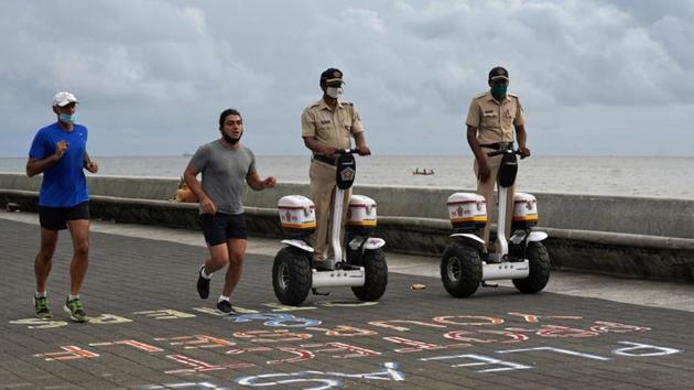 Police officers patrol on Segways as men wearing protective face masks run along the promenade at Marine Drive, after authorities eased lockdown restrictions that were imposed to slow the spread of the coronavirus disease (Covid-19), in Mumbai.(REUTERS) Police officers patrol on Segways as men wearing protective face masks run along the promenade at Marine Drive, after authorities eased lockdown restrictions that were imposed to slow the spread of the coronavirus disease (Covid-19), in Mumbai.(REUTERS)