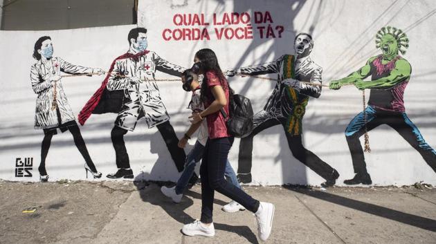 Pedestrians walk past a mural depicting a tug-of-war between health workers and Brazil’s President Jair Bolsonaro, aided by a cartoon-styled coronavirus with a message that reads in Portuguese: “Which side are you on?,” in Sao Paulo on June 19. Brazil crossed 1 million coronavirus cases on June 19, becoming only the second nation to do so after the US. (Andre Penner / AP) Pedestrians walk past a mural depicting a tug-of-war between health workers and Brazil’s President Jair Bolsonaro, aided by a cartoon-styled coronavirus with a message that reads in Portuguese: “Which side are you on?,” in Sao Paulo on June 19. Brazil crossed 1 million coronavirus cases on June 19, becoming only the second nation to do so after the US. (Andre Penner / AP)