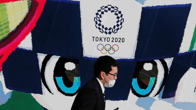 A man wearing a protective mask walks past a large poster featuring Tokyo 2020 Olympic Games mascot Miraitowa.(REUTERS)
