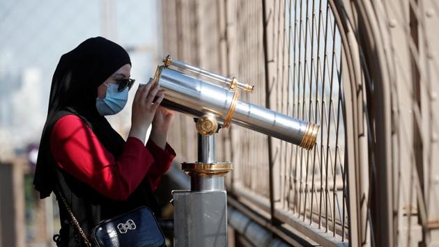 A woman wearing a protective face mask looks through a viewing telescope atop the Eiffel Tower on June 25. Managers told Reuters that they hope to get operations fully back to normal later this summer. (Charles Platiau / REUTERS)