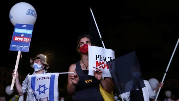 A demonstrator wearing a protective face mask holds flags during a protest against Israel's planned annexation of parts of the occupied West Bank, and over unemployment and economic issues, in Tel Aviv, Israel. (REUTERS) A demonstrator wearing a protective face mask holds flags during a protest against Israel's planned annexation of parts of the occupied West Bank, and over unemployment and economic issues, in Tel Aviv, Israel. (REUTERS)