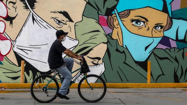 A man ride a bike past a coronavirus related mural by urban artists Mick Martinez and “Were Torres” depicting health care workers in Ciudad Juarez, Mexico on June 27. Responses to the coronavirus have varied across the world, defined initially in part by ideological stances but eventually following the needs of the medical urgencies presented by Covid-19. (Herika Martinez / AFP)