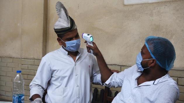 A server wearing a face mask and gloves is thermal screened at the Indian Coffee House on July 2. Each customer was being checked by a waiter, donning the usual white uniform and the headgear, with thermal scanners. (Samir Jana / HT Photo)