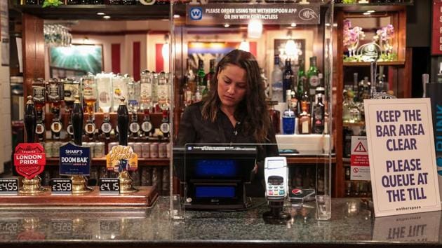 An employee works the till behind a perspex screen at The Moon Under Water pub in London on July 4. In addition to the reopening of much of the hospitality sector, couples can tie the knot once again, people can go and see a movie at their local cinema and many of those who have had enough of their lockdown hair can finally get a trim. In all cases, social distancing rules have to be followed. (Simon Dawson / Bloomberg)
