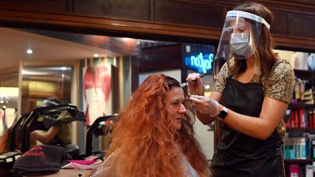 A hair stylist wearing a Personal Protective Equipment (PPE) face visor cuts a customers hair at a salon in Birkenhead on July 4. In other countries, the reopening of bars and restaurants has been blamed for a spike in infections, the AP reported. (Paul ELLIS / AFP)