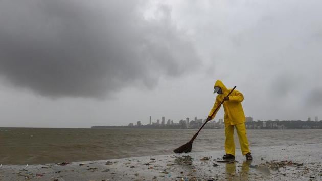 A municipal worker cleans garabage washed ashore by waves crashing Marine Drive promenade, during high tide, in Mumbai, Sunday, July 5, 2020. (PTI)