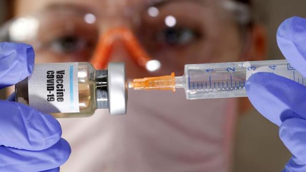 A woman holds a small bottle labelled with a ‘Vaccine Covid-19’ sticker and a medical syringe in this illustration.(Reuters File Photo)