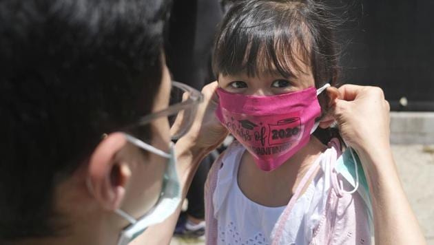Olivia Chan's father helps her with a new mask she received during a graduation ceremony for her Pre-K class in front of Bradford School in Jersey City. (AP) Olivia Chan's father helps her with a new mask she received during a graduation ceremony for her Pre-K class in front of Bradford School in Jersey City. (AP)