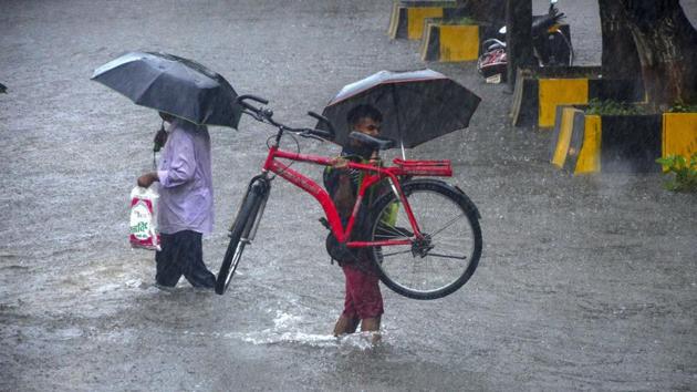 Commuters cross a waterlogged street during heavy rainfall, at Vashi in Navi Mumbai, Sunday, July 5, 2020. (PTI)
