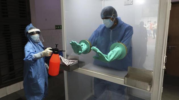 A health worker sanities the gloves of another inside a booth after he collects sample of a person for Covid-19 test at a hospital in New Delhi, on Monday. (AP Photo) A health worker sanities the gloves of another inside a booth after he collects sample of a person for Covid-19 test at a hospital in New Delhi, on Monday. (AP Photo)
