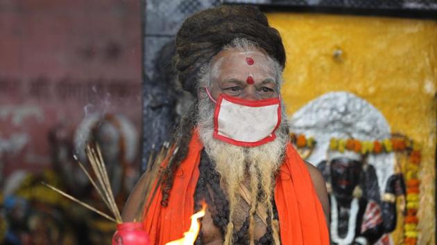 An Indian priest covers his face with a mask as a precaution against coronavirus and prays at a temple, in Prayagraj, India.(AP)