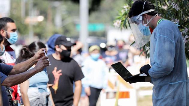 A testing associate dressed in personal protective equipment (PPE) helps people waiting in line to check in at a COVID-19 testing centre at Lincoln Park on July 7. Authorities have reported alarming upswings of daily caseloads in roughly two dozen states over the past two weeks, a sign that efforts to control transmission of the novel coronavirus have failed in large swaths of the country. (Mario Tama / AFP)