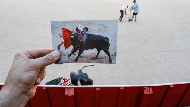 Nazca holds a picture of Spanish bullfighter Pablo Aguado driving the sword into a bull during a bullfight at the San Fermin festival, taken in July 2019. In the backdrop from now, is a Spanish apprentice bullfighter and a worker painting lines in the arena on July 7.  (Jon Nazca / REUTERS) 
