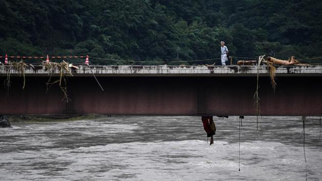 A man walks across a bridge covered with debris in Kuma village on July 9. AFP reported that in many areas, landslides reduced houses to rubble and floodwater rushed into homes in low-lying areas, destroying the contents and rendering them uninhabitable. (CHARLY TRIBALLEAU / AFP)