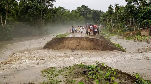People standing on an embankment after part of it was washed away by floodwaters in Pathsala on July 12. Nearly 13 lakh people in 24 of the state’s 31 districts have been affected by floods HT reported, citing the ASDMA report. (PTI)