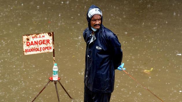 A municipal worker stands next to a sign warning of an open manhole on a flooded road to guide vehicles during rain in Mumbai on July 15. Heavy to very heavy rain this monsoon season has led Mumbai past its July average for rainfall, with half the month still ahead of it. (Sujit Jaiswal / AFP) A municipal worker stands next to a sign warning of an open manhole on a flooded road to guide vehicles during rain in Mumbai on July 15. Heavy to very heavy rain this monsoon season has led Mumbai past its July average for rainfall, with half the month still ahead of it. (Sujit Jaiswal / AFP)