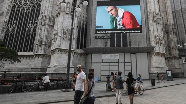 Pedestrians pass by a screen on the Duomo cathedral, showing a Moschino model during the Milan Digital Fashion Week, in Milan, Italy, Tuesday, July 14, 2020.(AP Photo/Luca Bruno)