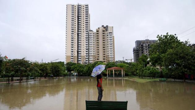 A man is seen holding an umbrella while standing on a bench in a waterlogged park in Sector 31, Noida on July 19. The monsoon reached Delhi and its adjoining areas on June 25, two days earlier than its usual date, but despite the early arrival rains had remained subdued so far. (Sunil Ghosh / HT Photo)