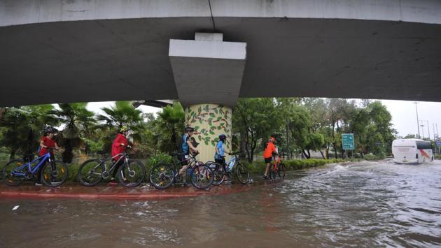 Cyclists move along a pavement next to a waterlogged road following heavy rain near Sector 44, in Noida on July 19. Weather forecasting agencies have said Delhi and its adjoining states of Punjab and Haryana are likely to experience continuous rainfall from July 19 as the monsoon trough is likely to shift to its normal position. (Sunil Ghosh / HT Photo)