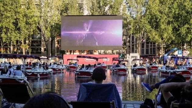 People watch the film Le Grand Bain seat on beach chairs and from boats at the Cinema on the water (Cinema sur l’eau) as a floating cinema with 38 socially-distant electric boats kicks off the Paris Plages summer event along the Bassin de la Villette, in Paris.(REUTERS/Gonzalo Fuentes)