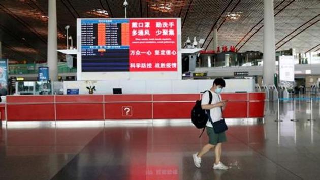 A man wearing a face mask walks past a counter with a display showing flight information and a message on preventive measures against the coronavirus disease (Covid-19), at the departure hall of Beijing Capital International Airport. (Reuters Photo)