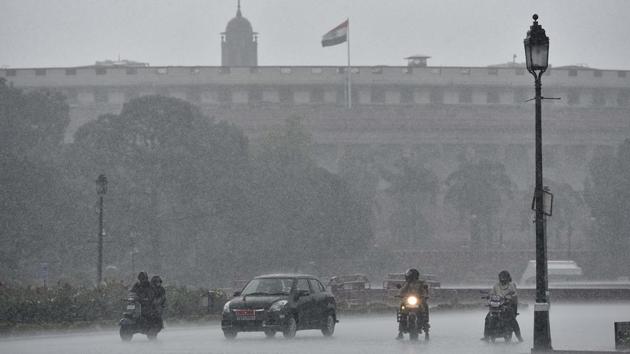 Commuters out in the rain at Vijay Chowk in New Delhi.(Sanjeev Verma/HT PHOTO)