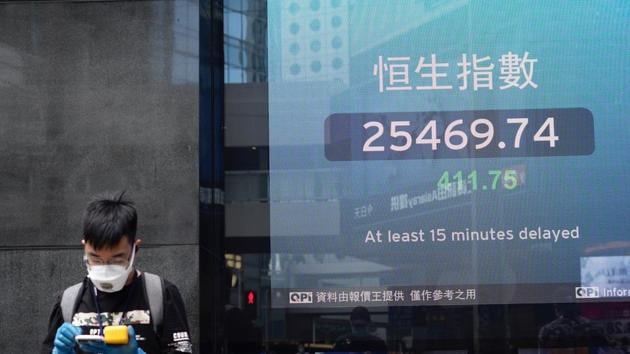 A man wearing a face mask stands next to a bank's electronic board showing the Hong Kong share index in Hong Kong on Tuesday. (AP File Photo) A man wearing a face mask stands next to a bank's electronic board showing the Hong Kong share index in Hong Kong on Tuesday. (AP File Photo)