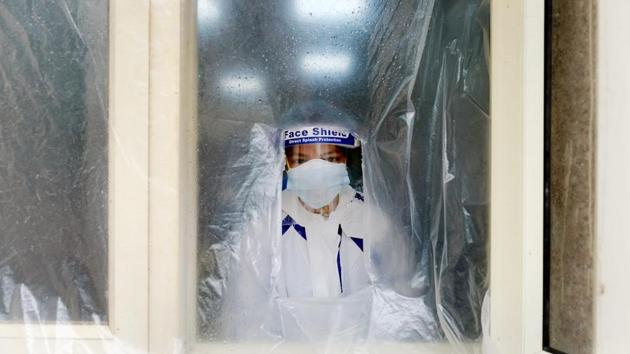 A health worker wearing personal protective equipment (PPE) stands behind a plastic screen at a rapid-antigen methodology Covid-19 testing centre set up at the Nehru Homeopathy Medical College and Hospital in New Delhi on Monday.(Bloomberg)