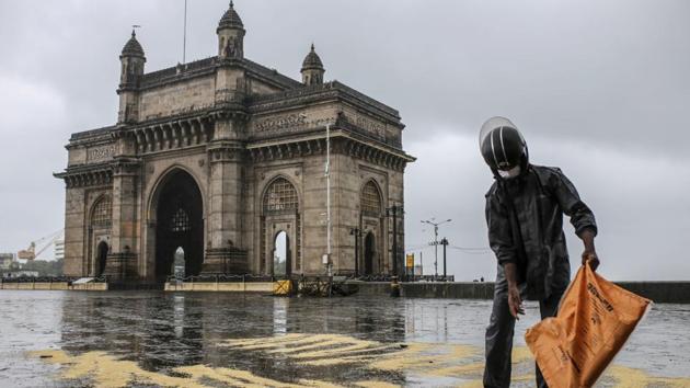 A man wearing a protective mask pours bird feed on to the ground at a deserted Gateway of India in Mumbai.(Bloomberg)