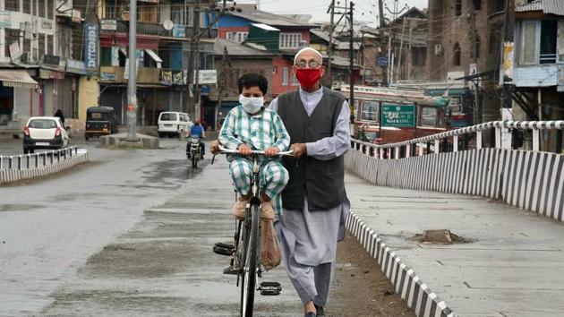 A man wearing face mask pulls his bicycle on a deserted road in Srinagar on Tuesday.(ANI Photo)