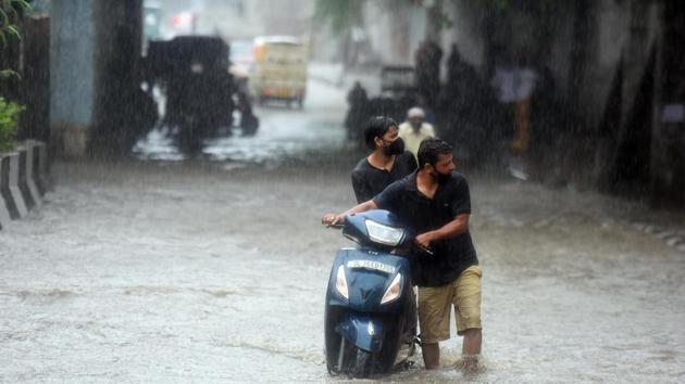 Commuters wade through a water-logged road during heavy rain near Mother Dairy plant, in New Delhi.(Raj K Raj/Mohd Zakir/ Hindustan Times)