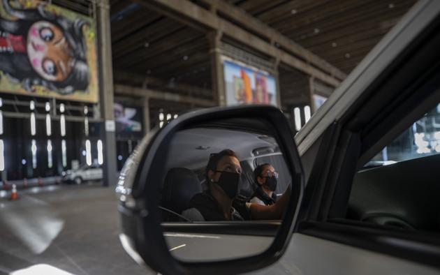Visitors take in an art exhibit from inside a car as they drive through a warehouse displaying paintings and photos in Sao Paulo, Brazil, Friday, July 24, 2020, amid the new coronavirus pandemic. (AP)