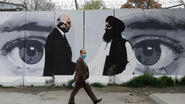 An Afghan man wearing a protective face mask walks past a wall painted with photo of Zalmay Khalilzad, US envoy for peace in Afghanistan, and Mullah Abdul Ghani Baradar, the leader of the Taliban delegation, in Kabul, Afghanistan.(REUTERS)