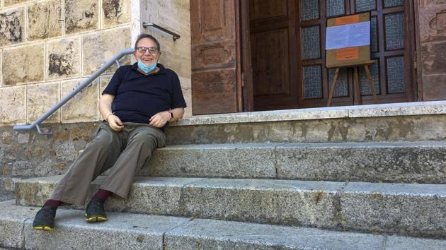 Rev. Lorenzo Pasquotti poses for photos on the steps of his church at the Giglio Island, Italy, Wednesday, June 24, 2020. Some 50 local mourners filled the pews for that funeral in Saints Lorenzo and Mamiliano Church, including a man from the continent that had Covid-19 infection, recalled the pastor, Rev. Pasquotti. “After the funeral, there were greetings, hugging and kissing,” as always. Then came the procession to the cemetery, where “there were more hugs and kisses.” Yet, “none of us had any sign” of Covid-19 in the days to follow, said Pasquotti. “No one was sick. No symptoms that can make you think you were infected.” (AP Photo/Paolo Santalucia)