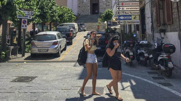 Two women walk in front of Saints Lorenzo and Mamiliano Church at the Giglio Island, Italy, Wednesday, June 24, 2020. (AP Photo/Paolo Santalucia)