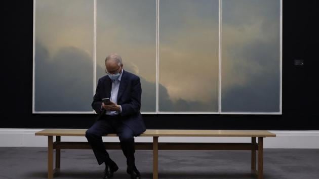 A man sits in front of a painting by Gerhard Richter called 'Wolken (fenster) (Clouds (window))' at Sotheby's auction rooms in London, Thursday, July 23, 2020. (AP Photo/Kirsty Wigglesworth)