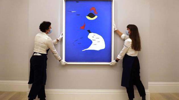 Sotheby's employees adjust a painting by Joan Miro called 'Peinture (Femme au chapeau rouge' at Sotheby's auction rooms in London, Thursday, July 23, 2020. (AP Photo/Kirsty Wigglesworth)