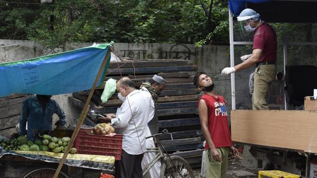 A man purchases vegetables while a health worker collects a swab sample from a man opposite him, in New Delhi on July 25. In contrast with the number of tests conducted over the week but in line with weekend figures, fewer tests were conducted on July 26 at 17,522. Delhi is currently just a fraction short of completing a million tests. (Arvind Yadav / HT Photo)