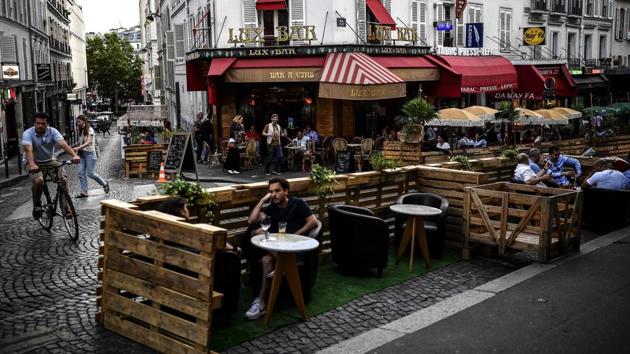 People have drinks at the extended terrace of a cafe made of wooden pallets in Paris on July 23. Following a loosening of Covid-19 lockdown regulations by the city hall, customers at cafes are now spread out on tables and chairs across parallel parking spaces, in a scene repeated throughout Paris. (Christophe Archambault / AFP)